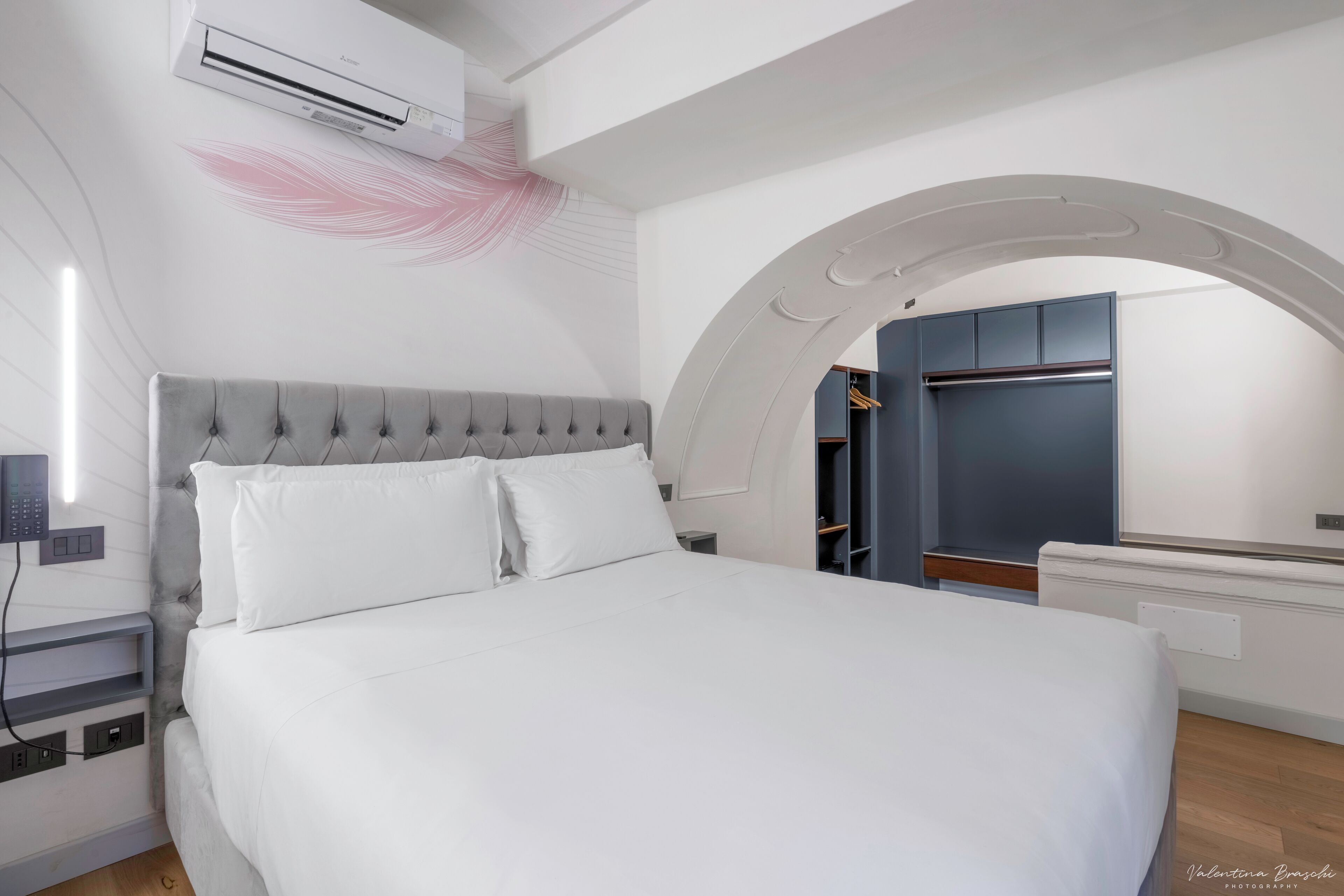 Une chambre à coucher moderne avec une tête de lit capitonnée, un couvre-lit blanc et un appareil de climatisation fixé au mur.