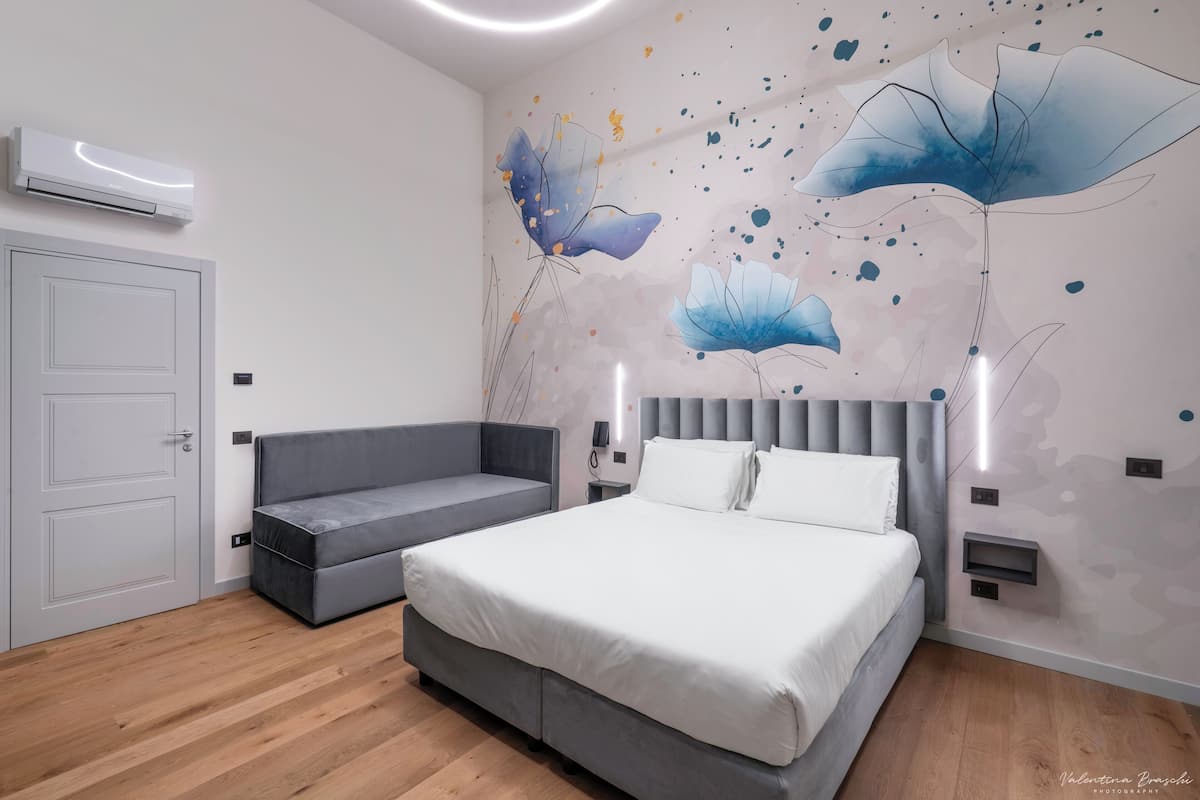Ein modernes Schlafzimmer mit einem Bett, einem grauen Sofa, einer weißen Tür und einer Wand mit abstrakter Blumenkunst.