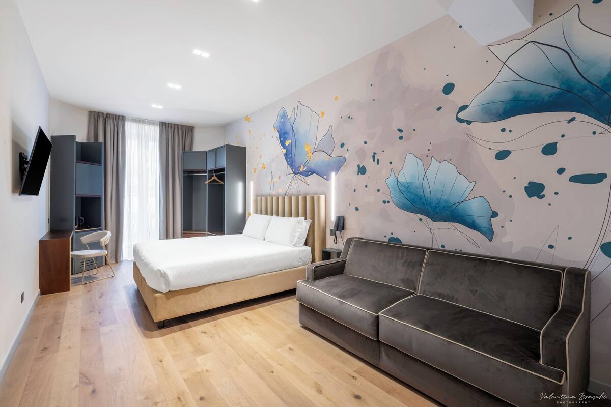 Ein modernes Hotelzimmer mit Bett, Sofa, Fernseher und Kleiderschrank.