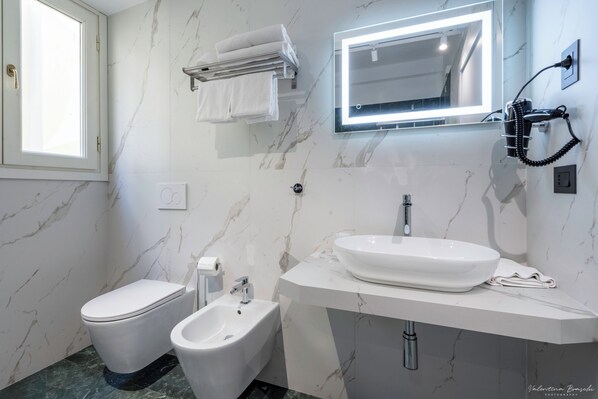 A modern bathroom with a toilet, bidet, and a large sink with a mirror above it.