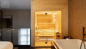 Ein modernes Hotelzimmer mit Sauna, Holzverkleidung, einer Duschkabine aus Glas und einem Bett mit einer beigen Tagesdecke.