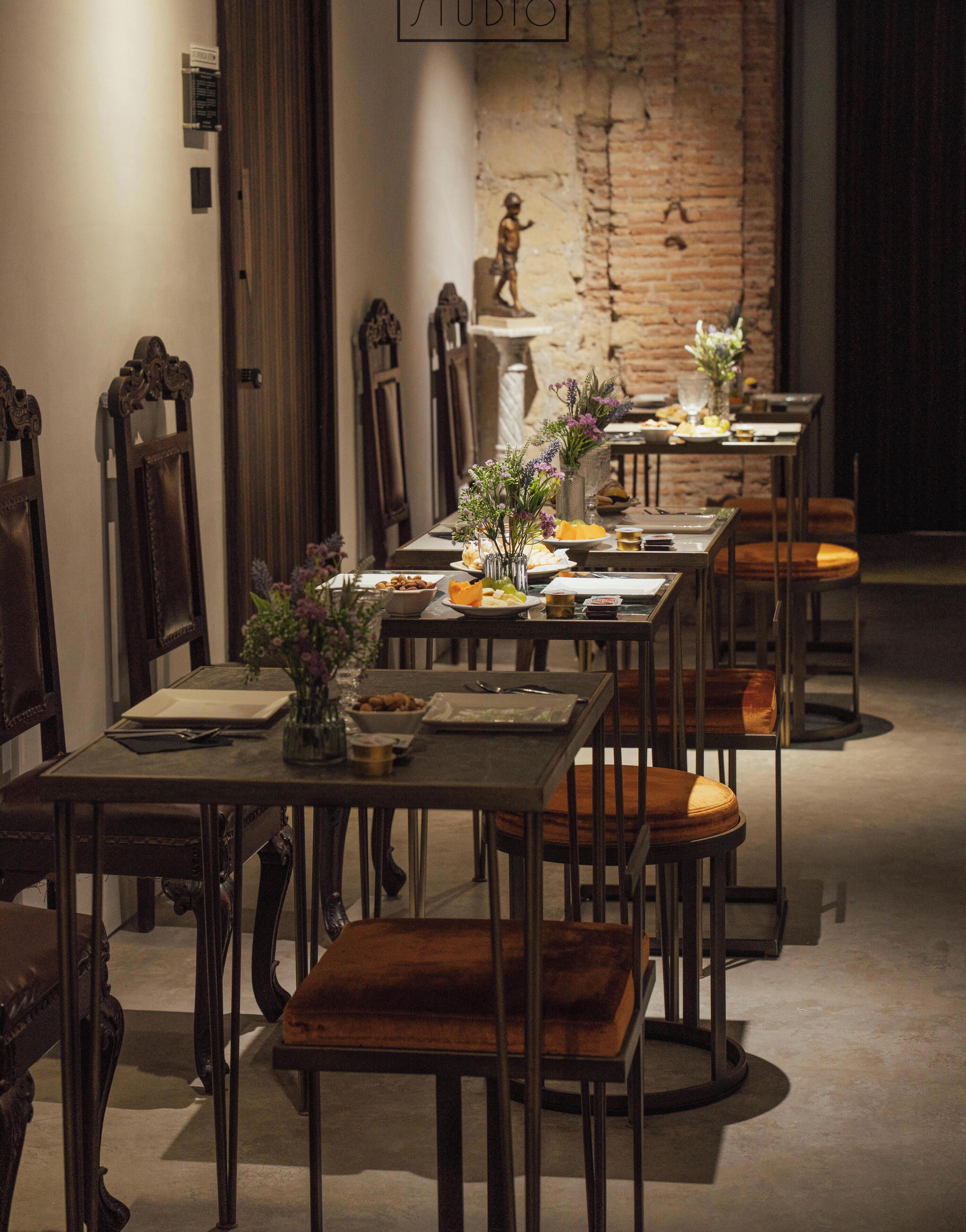 Un comedor con mesas dispuestas para una comida, sillas y una estatua al fondo.