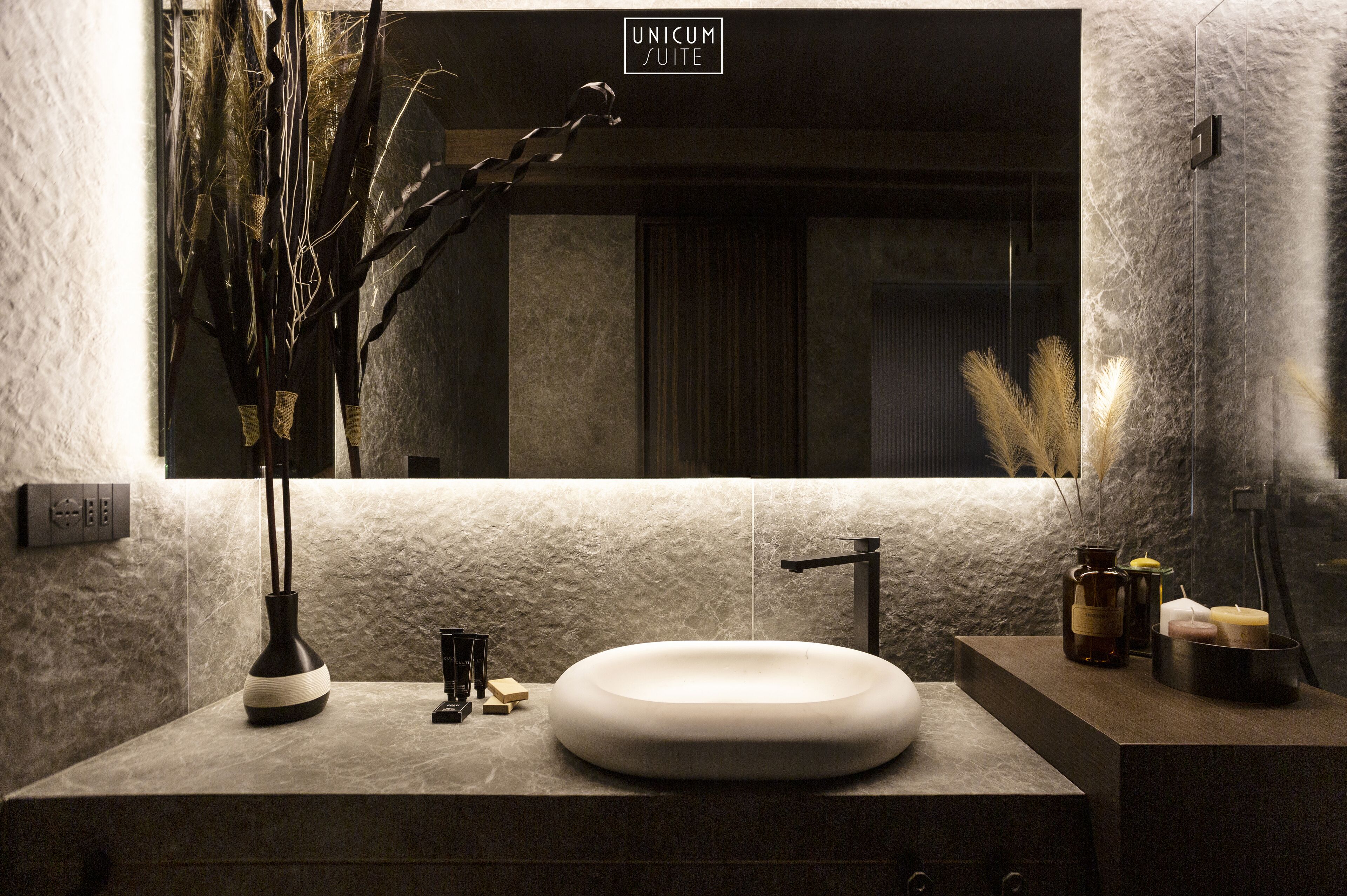 A modern bathroom with a large mirror, a round sink, and a textured wall.