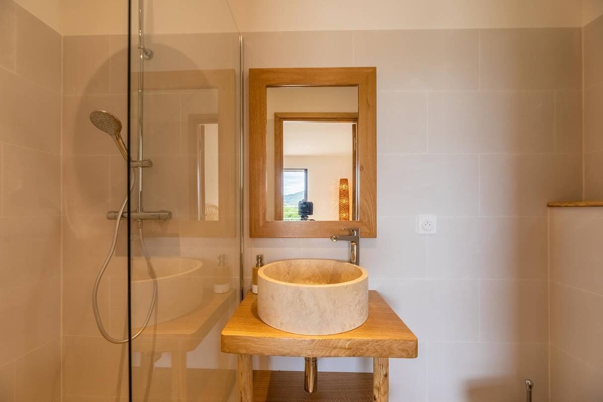Ein Badezimmer mit einer Duschkabine aus Glas, einem Holzwaschtisch mit runder Spüle und einem Spiegel über dem Waschbecken.