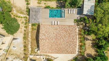 Vista aérea de un resort con piscina, terraza de madera y zona cubierta con sillas de descanso.