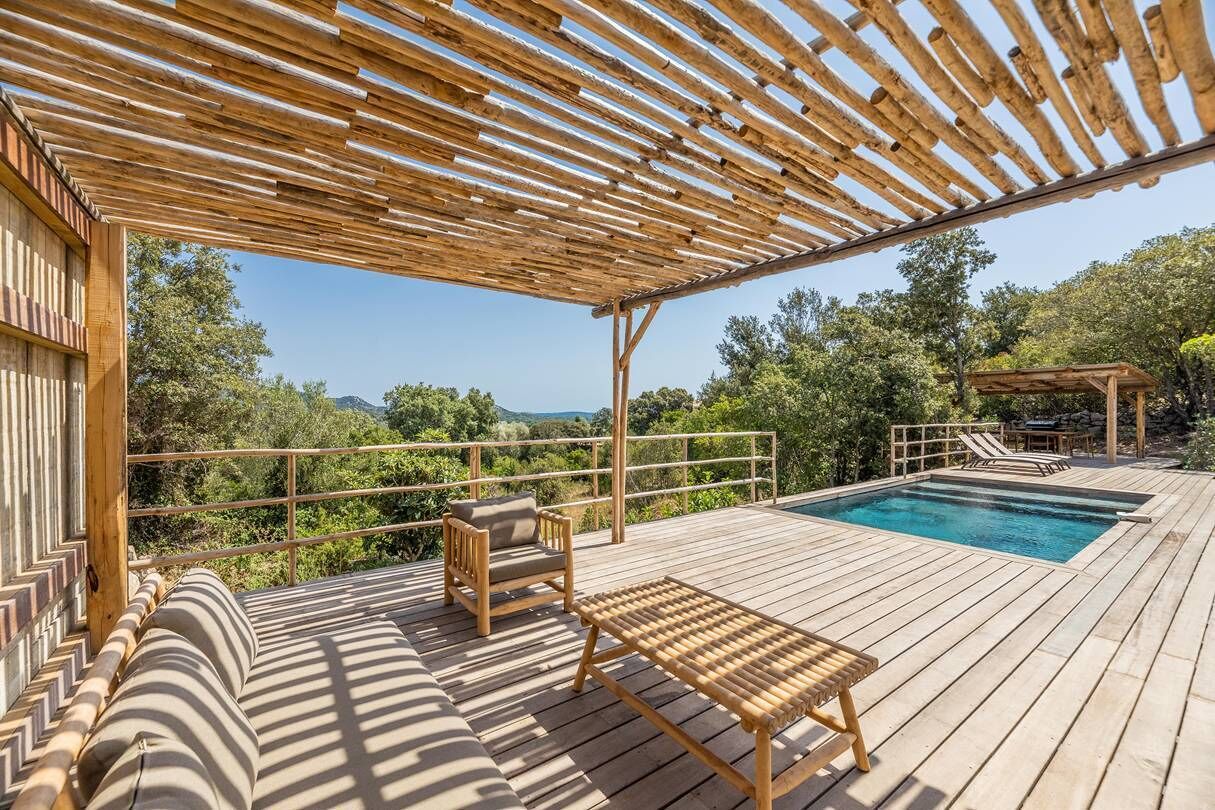 A wooden deck with a pool, outdoor seating, and a pergola.