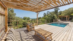 A wooden deck with a pool, outdoor seating, and a pergola.