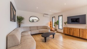 A modern living room with a curved sectional sofa, a black coffee table, a wooden TV stand, and a large mirror on the wall.