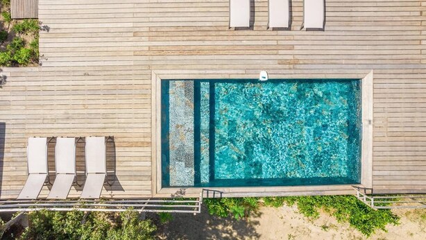 An aerial view of a wooden deck with a rectangular pool, surrounded by lounge chairs and a small staircase.