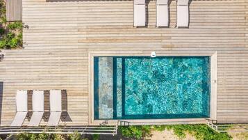 An aerial view of a wooden deck with a rectangular pool, surrounded by lounge chairs and a small staircase.