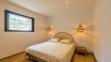 A bedroom with a bed, a window, and two wall-mounted lamps.