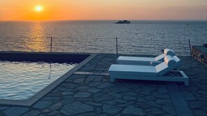 A sunset view from a poolside area with lounge chairs and a stone deck.