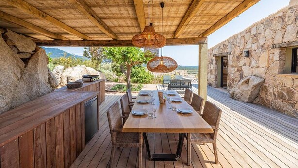 An outdoor dining area with a wooden table set for six, surrounded by wicker chairs, under a wooden pergola with hanging rattan lamps. - Bergerie mountain view heated swimming pool (SOTTA)