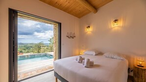 A bedroom with a large bed, a view of a swimming pool, and a wooden ceiling. - Bergerie mountain view heated swimming pool (SOTTA)