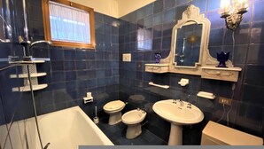 Une salle de bain avec une baignoire, deux toilettes, un bidet, un lavabo et un miroir.