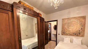 Une chambre avec une grande armoire en bois, un lit avec une literie blanche, un lustre et une peinture abstraite moderne accrochée au mur.