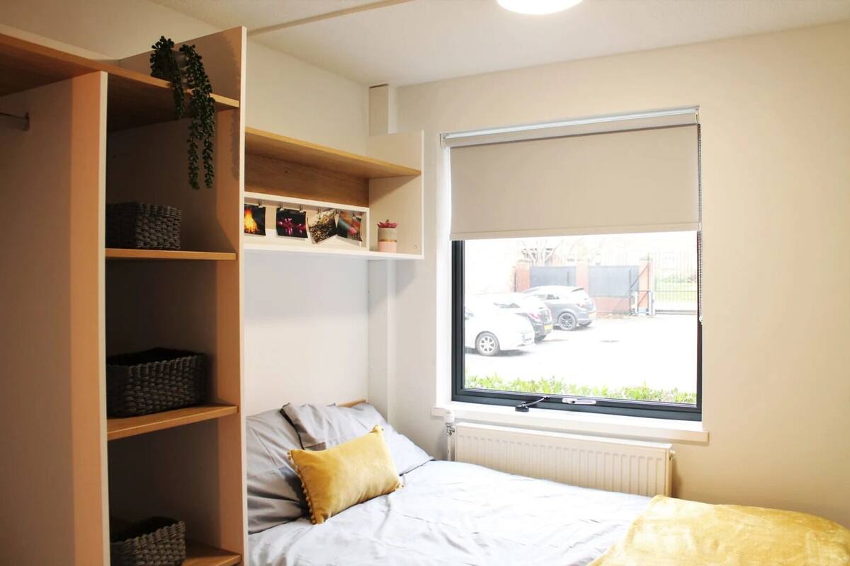 A bedroom with a bed, a window with a view of parked cars, and built-in shelving with baskets.