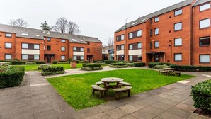 A courtyard with a central lawn, surrounded by brick buildings with multiple windows and a reception area. - For Students Only Regents Court in Leicester (Leicester)