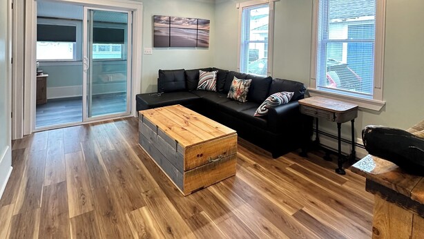 Un salon moderne avec un plafond en bois, un canapé d’angle noir, une table basse en bois et une petite table avec un tiroir.