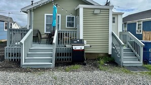 Une maison de plain-pied avec un porche, une petite terrasse et une poubelle.