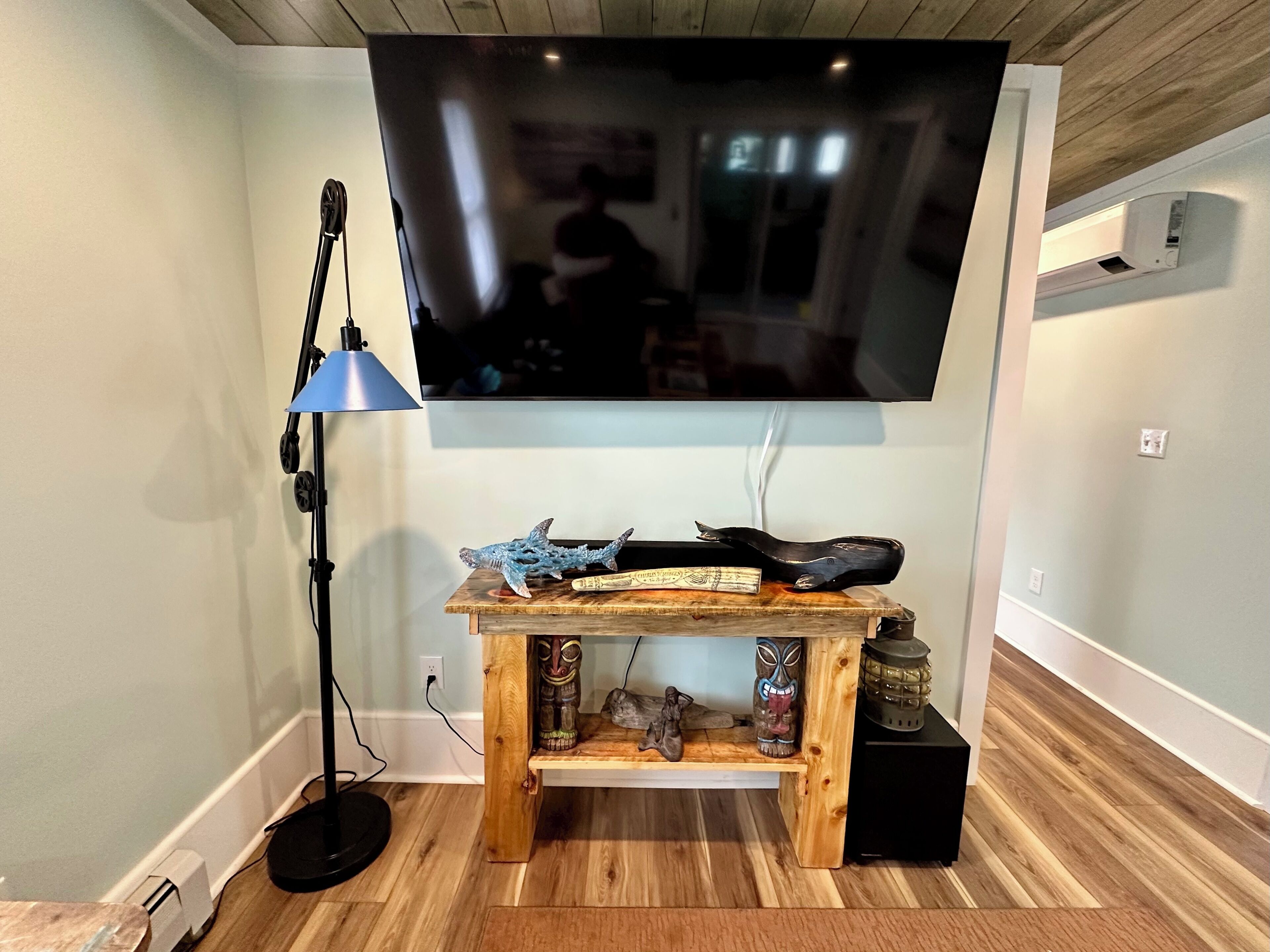 Een woonkamer met een flatscreen televisie aan de muur, een houten salontafel met decoratieve objecten, een vloerlamp en een zwarte speaker.