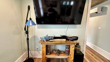 Een woonkamer met een flatscreen televisie aan de muur, een houten salontafel met decoratieve objecten, een vloerlamp en een zwarte speaker.