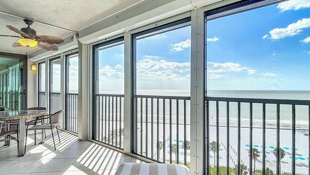 Un balcón con vista a la playa, una mesa con sillas y un ventilador de techo.