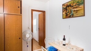 Ein kleiner Raum mit einem Holzschrank, einem Ventilator, einem Tisch mit einer Weinflasche und einem Bild an der Wand.