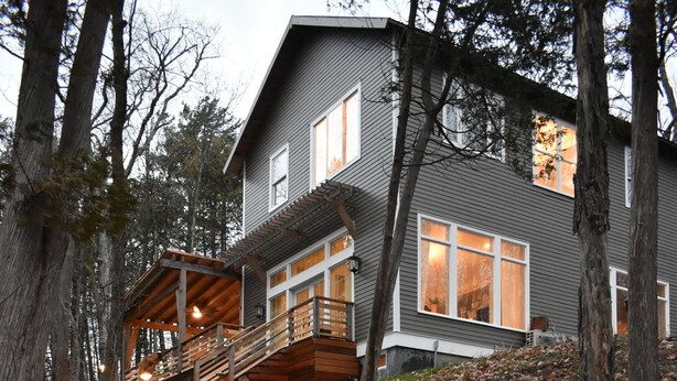 Une maison avec un escalier en pierre menant à une terrasse en bois, entourée d’arbres et de feuilles d’automne.