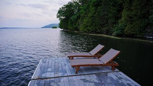 Une jetée en bois, agrémentée de deux chaises longues, fait face à un lac paisible, le tout étant entouré d’une végétation luxuriante et de collines lointaines.