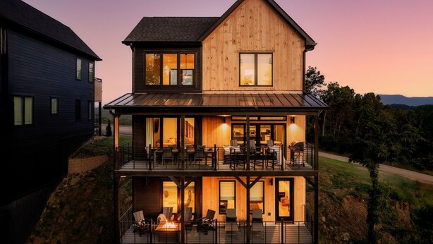Een houten huis met twee verdiepingen, een balkon, een open haard en uitzicht op het omliggende landschap.