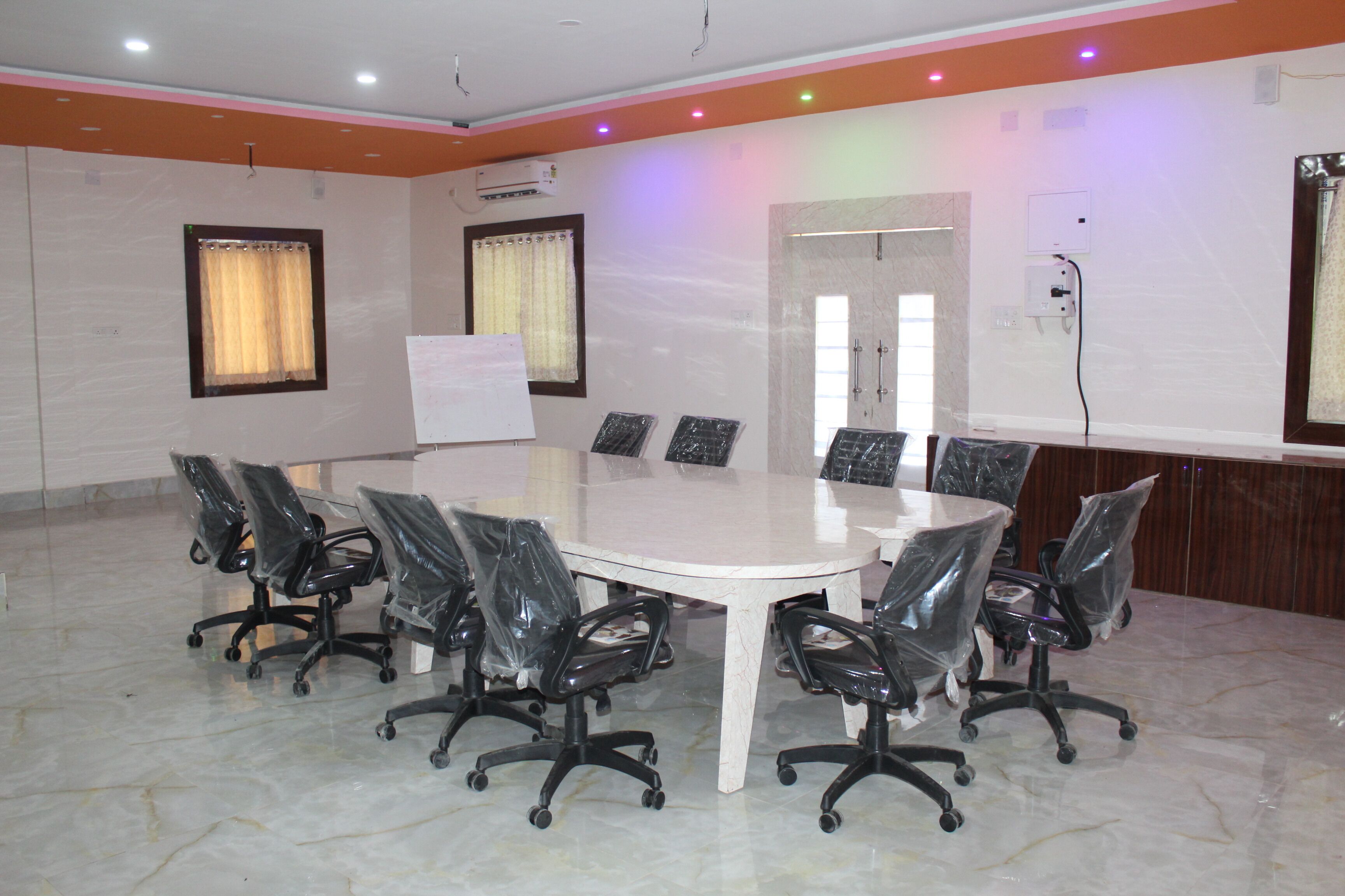 A conference room with a large oval table, eight chairs, and a whiteboard.