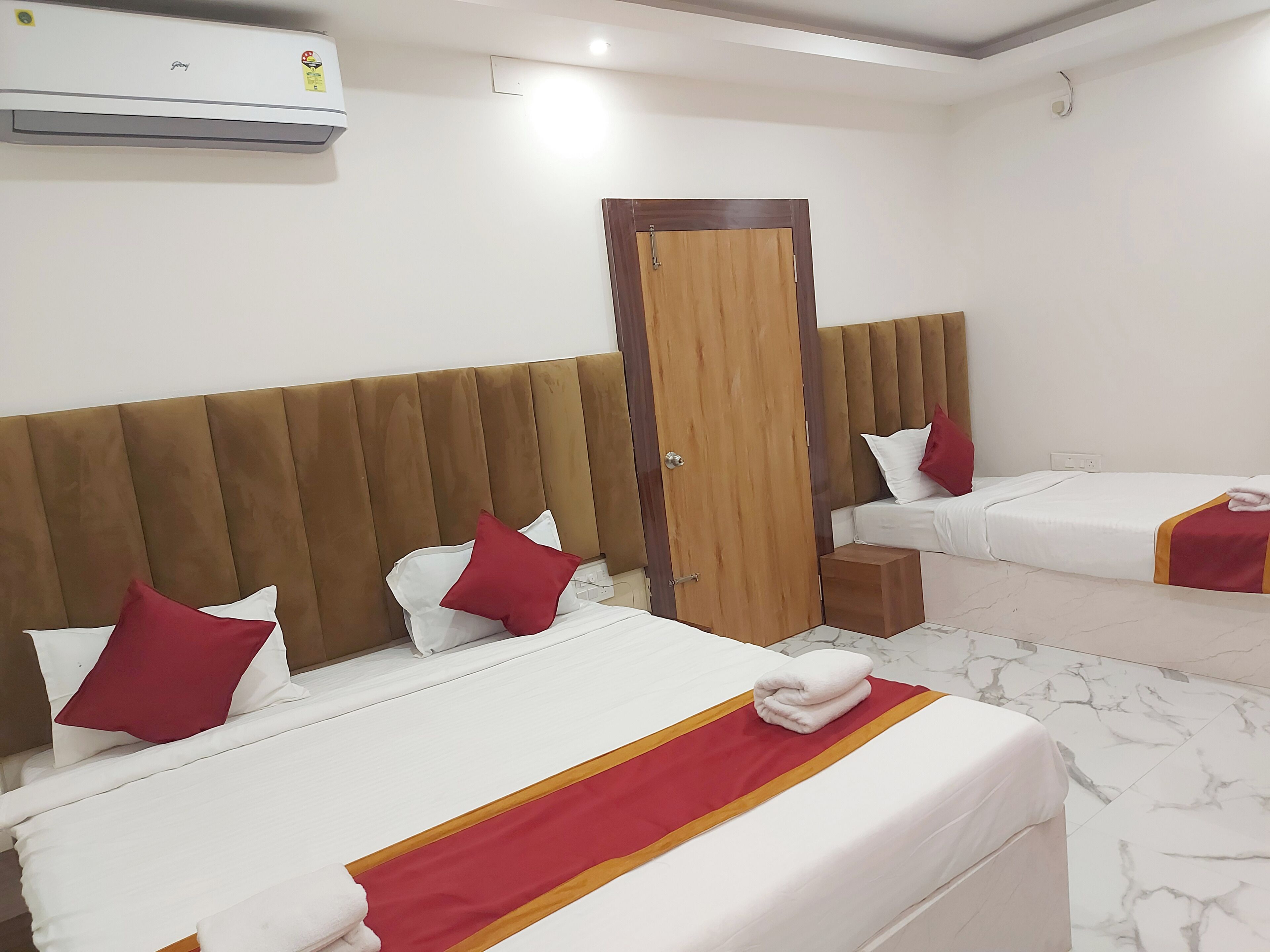 Ein Hotelzimmer mit zwei Betten, jeweils mit weißer Bettwäsche und roten Akzenten, einem Holz-Kopfteil und einer Holztür.