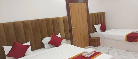 Quarto de hotel com duas camas, cada uma com roupa de cama branca e detalhes vermelhos, cabeceira de madeira e porta de madeira.