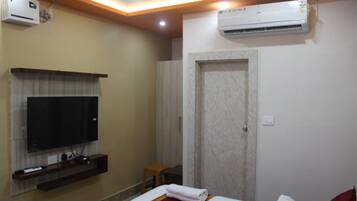 A hotel room with a television mounted on the wall, a bed with a red accent, an air conditioning unit, and a door with a marble-like texture.