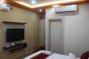 A hotel room with a television mounted on the wall, a bed with a red accent, an air conditioning unit, and a door with a marble-like texture.