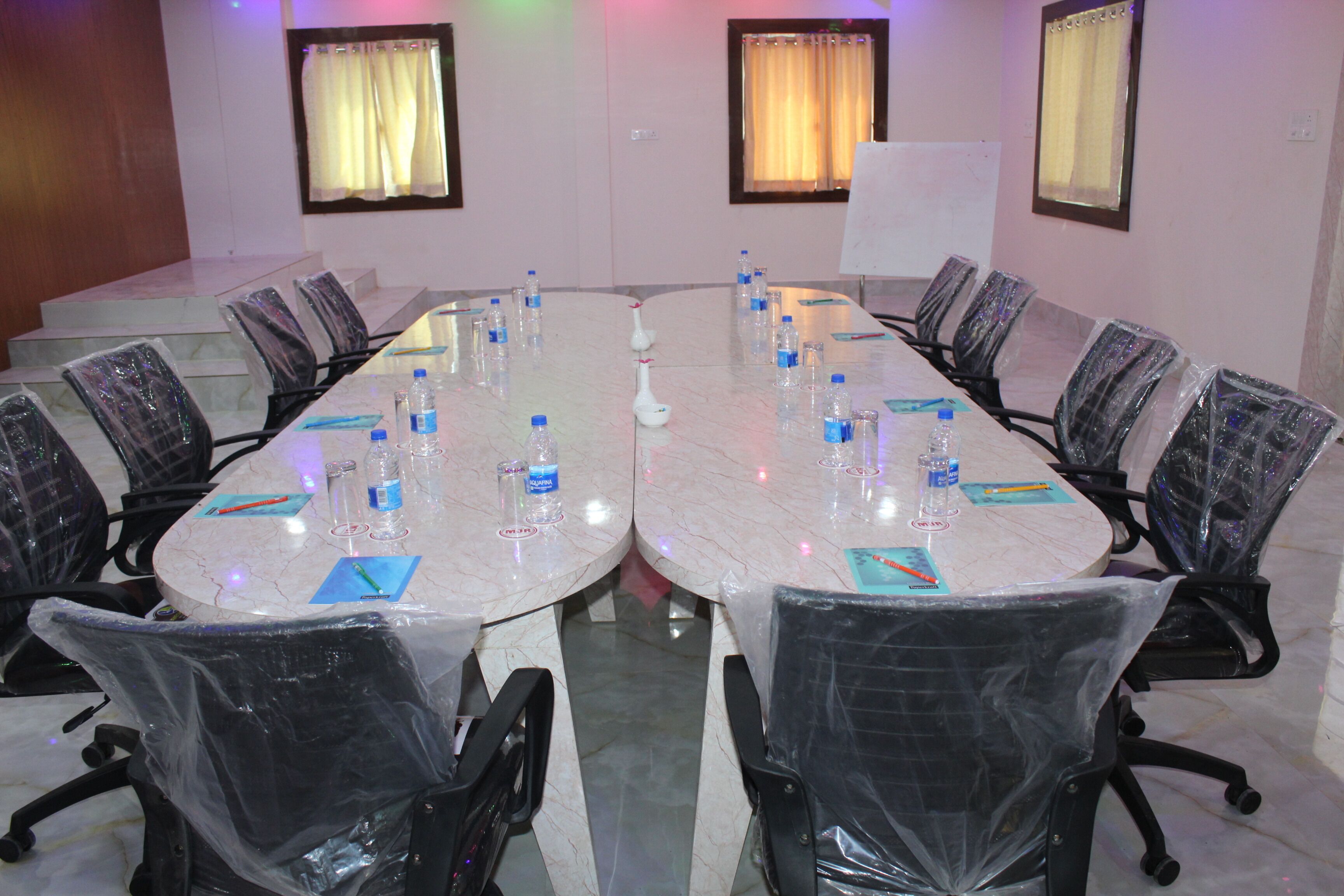 Una sala de conferencias con una gran mesa ovalada, rodeada de sillas con cubiertas protectoras y botellas de agua sobre la mesa.