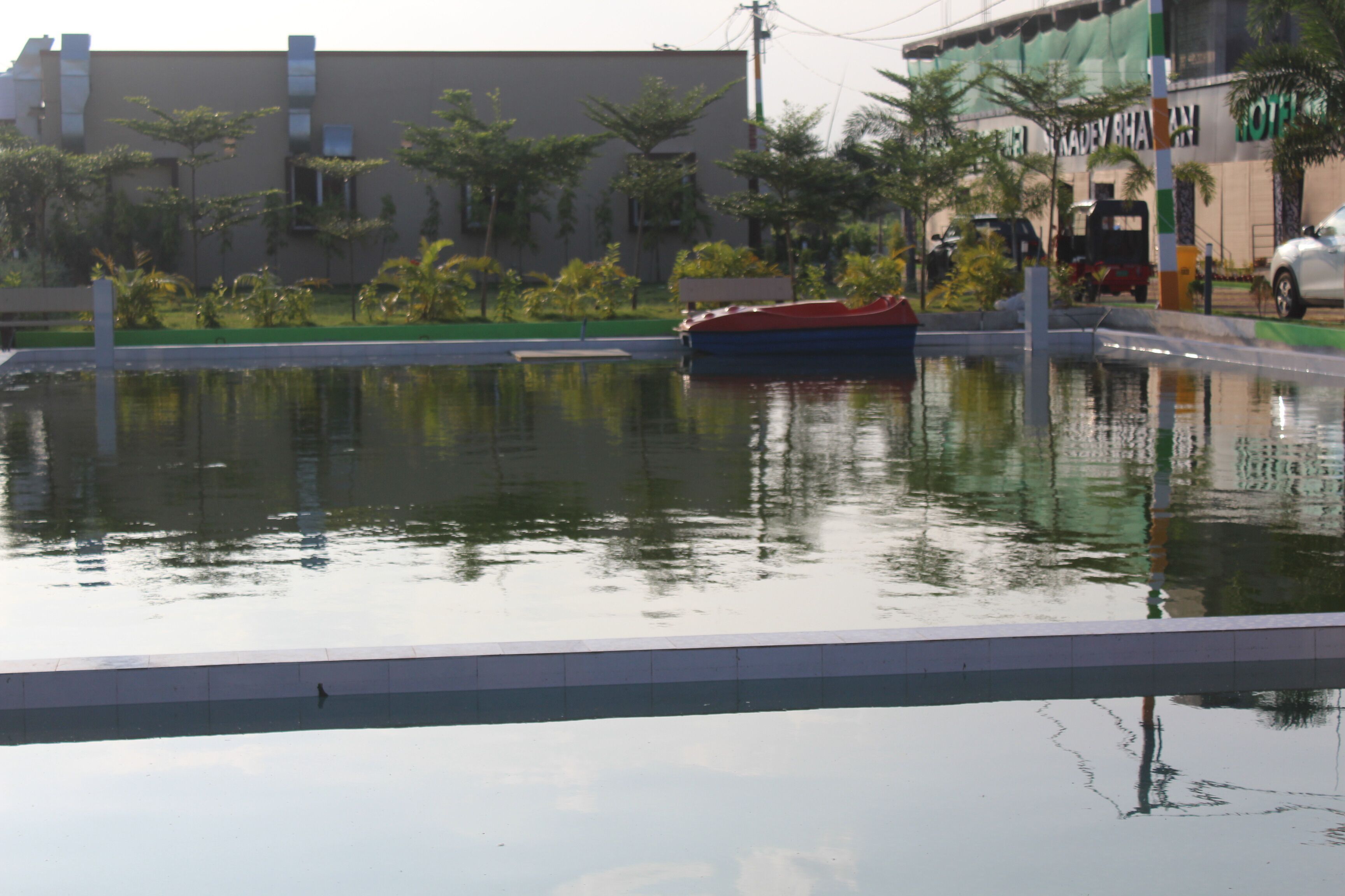 A swimming pool with a boat, surrounded by greenery and buildings.