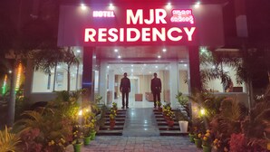 Ein Hotel Eingang mit einem Schild, auf dem 'HOTEL MJR RESIDENCY' steht, und zwei Personen, die am Eingang stehen.