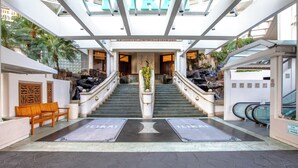A hotel lobby with a central staircase, wooden benches, a reception desk, and a view of the sky through a glass ceiling. - Ocean View Waikiki Retreat at the Iconic Ilikai Hotel Near Beach and Ala Moana (Honolulu)