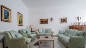 A living room with four green upholstered sofas arranged around a central coffee table, a lamp, and framed artwork on the walls.