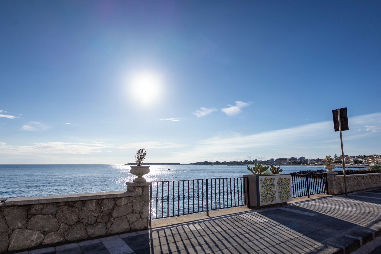 Een promenade aan het water met een stenen balustrade, een metalen hek en een bloempot.