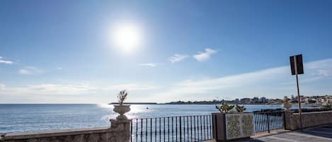 A waterfront promenade with a stone balustrade, a metal fence, and a potted plant.