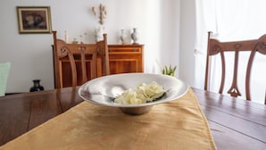 A dining table with a bowl of food, wooden chairs, a wooden cabinet, and a framed picture on the wall.