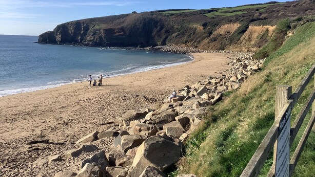 Una playa costera con terreno rocoso y una valla de madera.