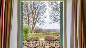 Una ventana con vistas a un muro de piedra y follaje verde.