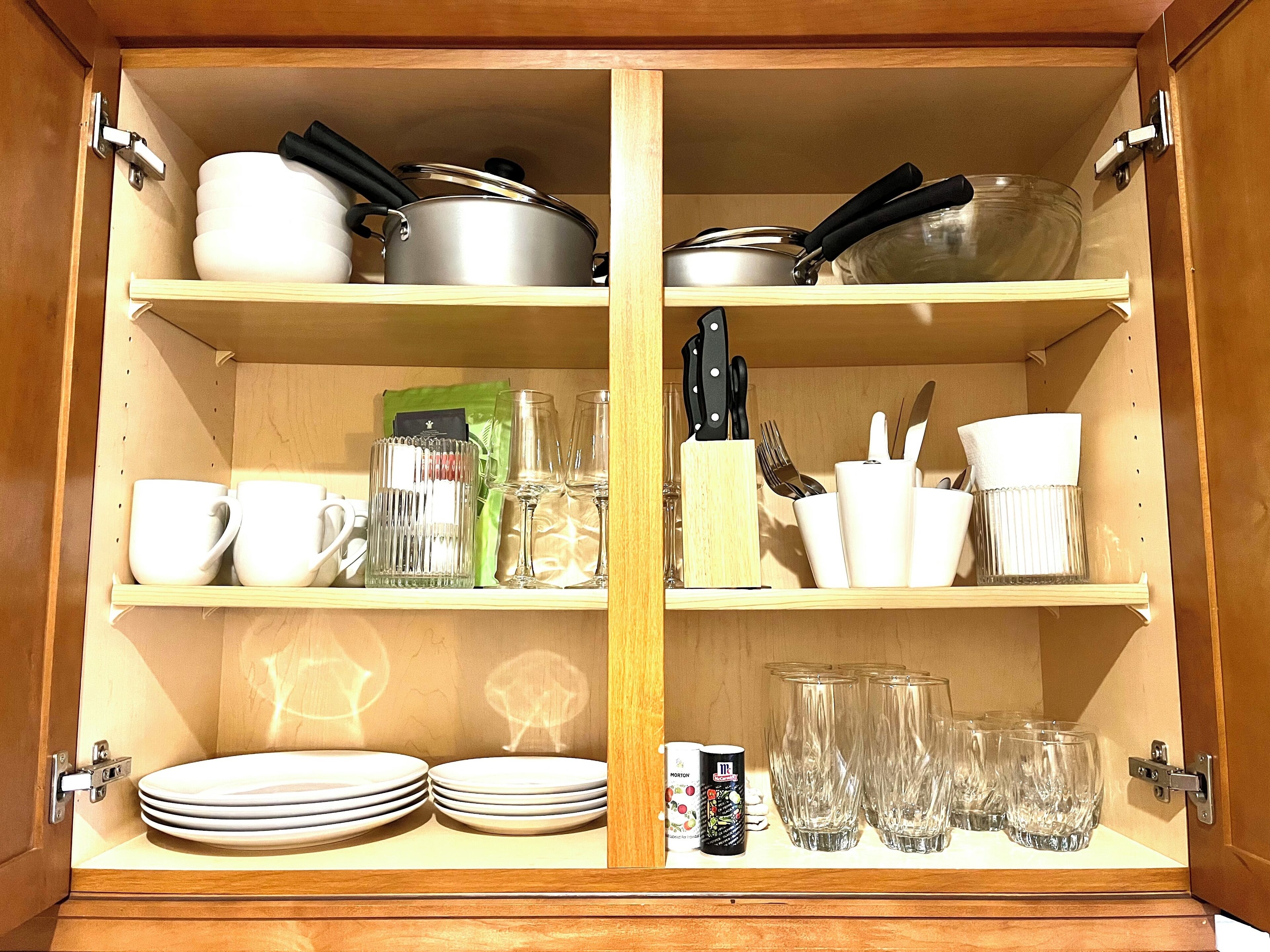 Un mueble de madera con estantes que contienen utensilios de cocina, como platos, tazas y vasos.