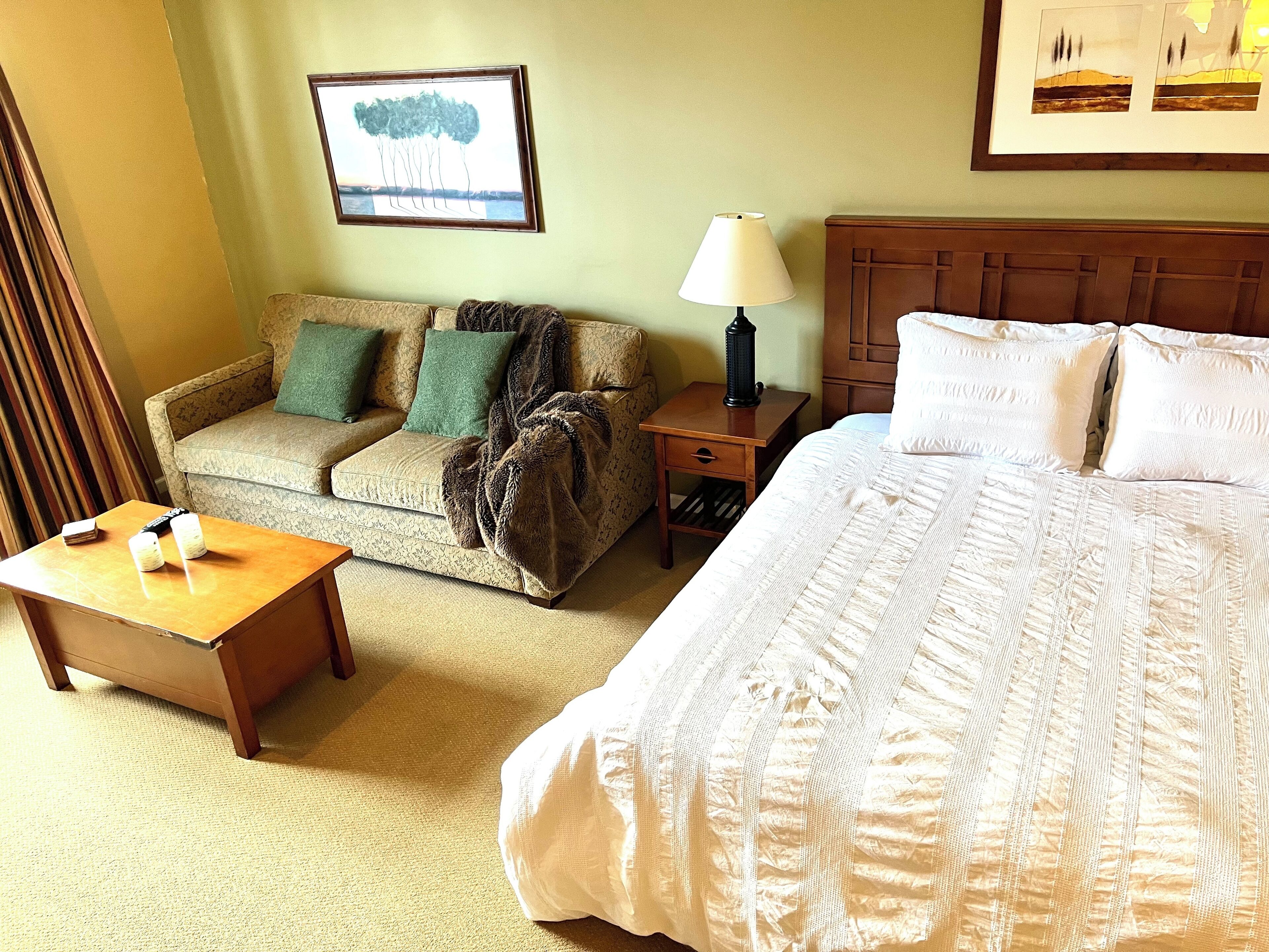 Une chambre d’hôtel avec un lit, un canapé, une table de chevet et une lampe.