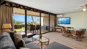 Un salón amplio con un gran ventanal corredera que da a un espacio exterior, un conjunto de sofás cómodos, una mesa de comedor con sillas y un ventilador de techo.