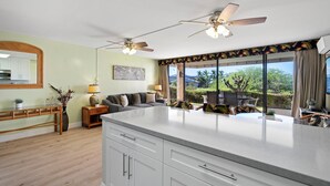 Una cocina moderna con una isla grande, dos ventiladores de techo y vistas al exterior.